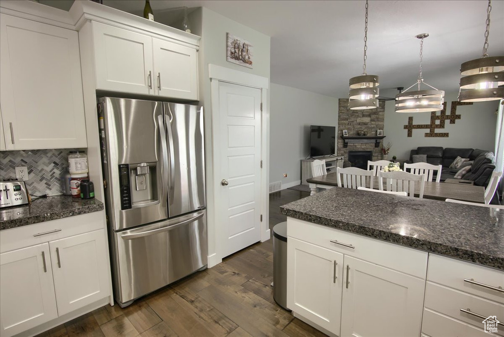 Kitchen featuring stainless steel fridge, backsplash, white cabinets, dark wood-style flooring, and a fireplace