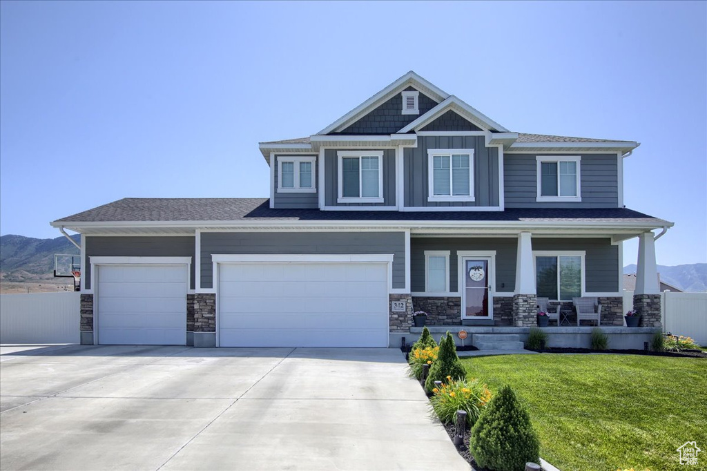 Craftsman house featuring covered porch, driveway, a mountain view, stone siding, and an attached garage