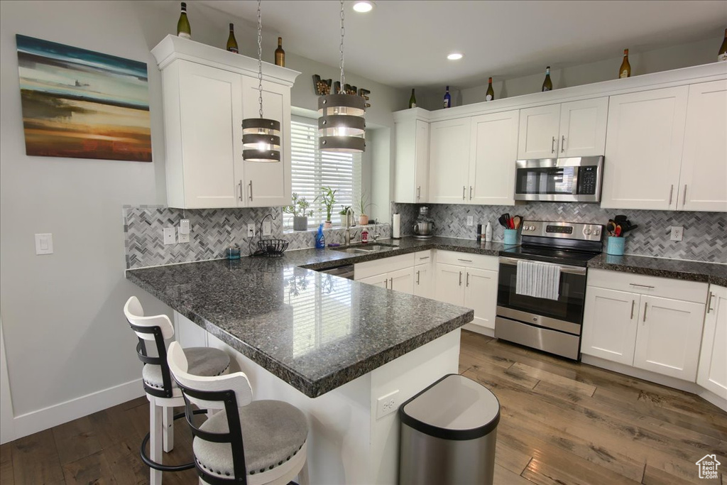 Kitchen featuring appliances with stainless steel finishes, white cabinets, backsplash, dark wood-style floors, and recessed lighting