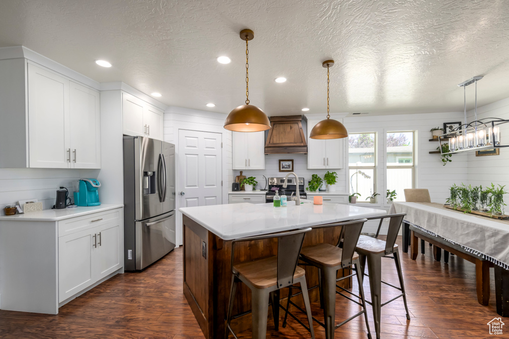 Kitchen featuring appliances with stainless steel finishes, premium range hood, light countertops, a kitchen breakfast bar, and a textured ceiling