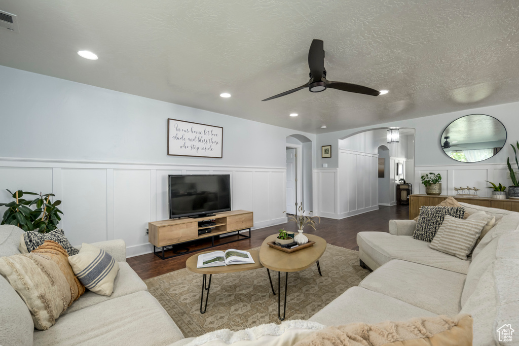 Living room featuring arched walkways, a decorative wall, a ceiling fan, wood finished floors, and a wainscoted wall