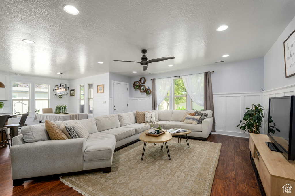 Living area with a decorative wall, dark wood-style floors, wainscoting, ceiling fan, and a textured ceiling