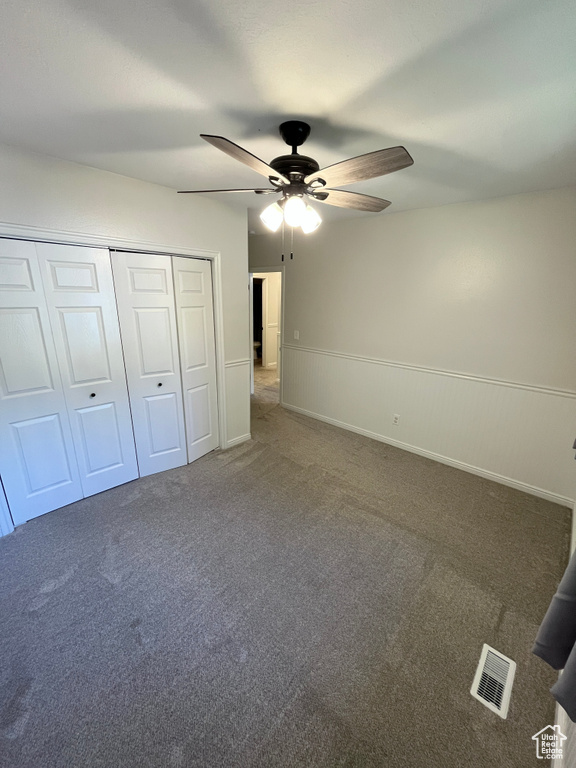 Unfurnished bedroom with wainscoting, carpet, a closet, and a ceiling fan