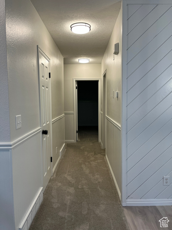 Corridor with a textured ceiling, carpet floors, and wainscoting