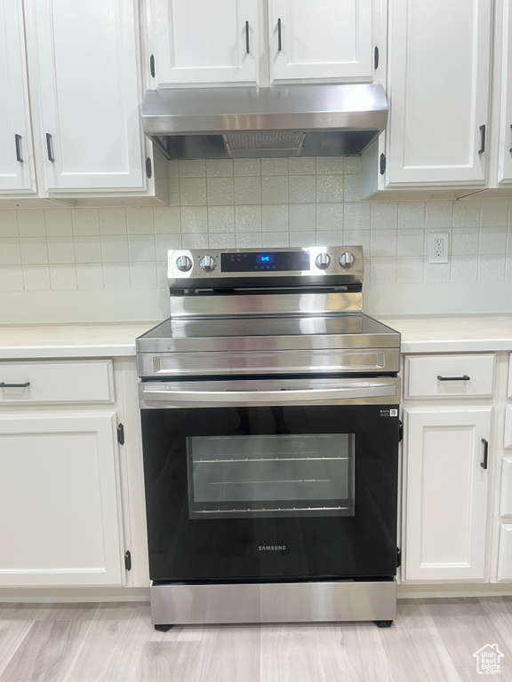 Kitchen with stainless steel electric stove, range hood, white cabinets, light countertops, and backsplash