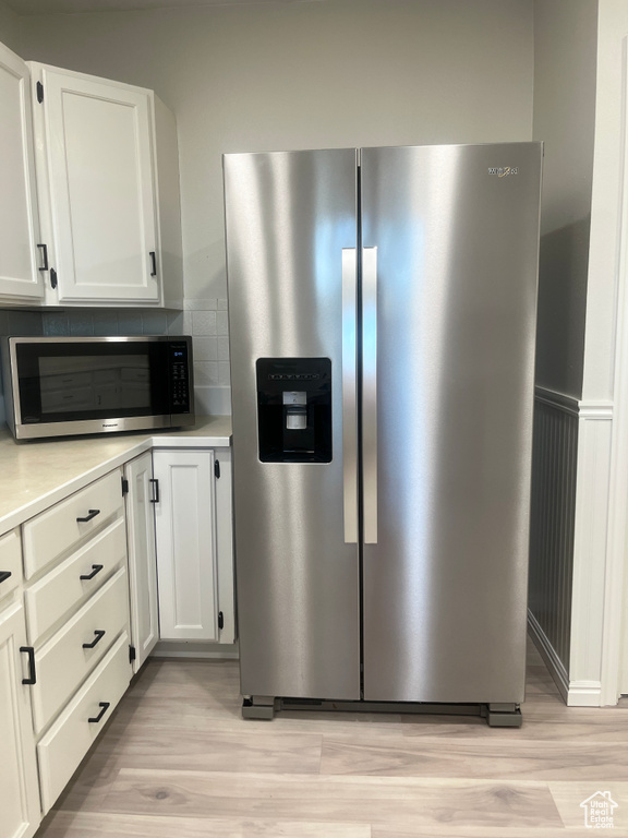 Kitchen with stainless steel appliances, light wood finished floors, light countertops, tasteful backsplash, and white cabinetry