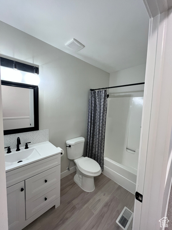 Bathroom featuring vanity, wood finished floors, shower / bath combination with curtain, and tasteful backsplash