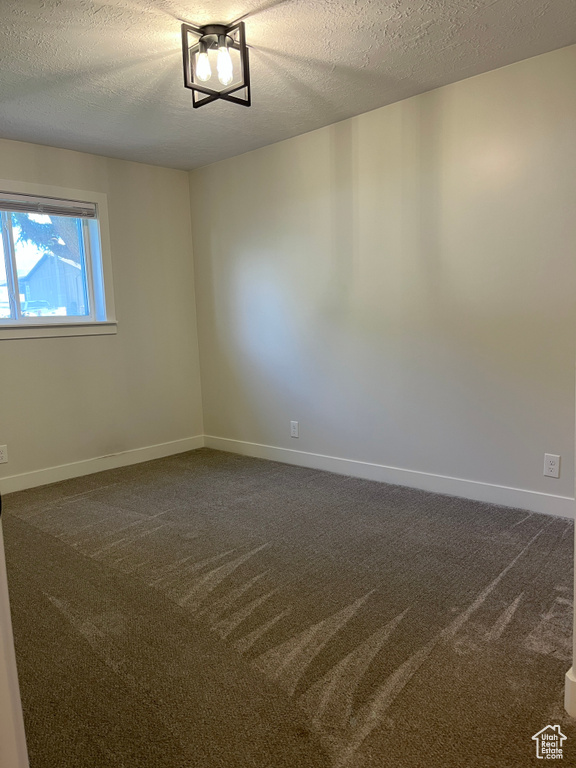 Empty room with dark colored carpet and a textured ceiling
