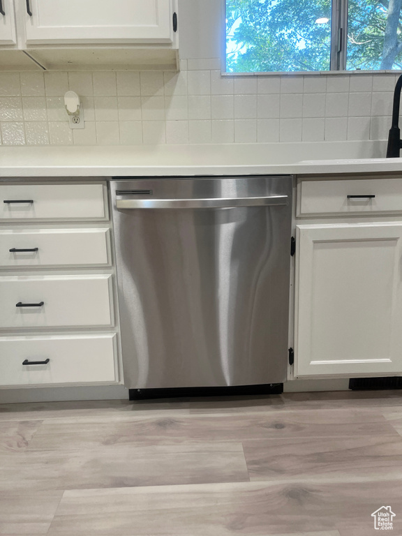 Kitchen view of dishwasher, backsplash, white cabinets, light countertops, and light wood finished floors