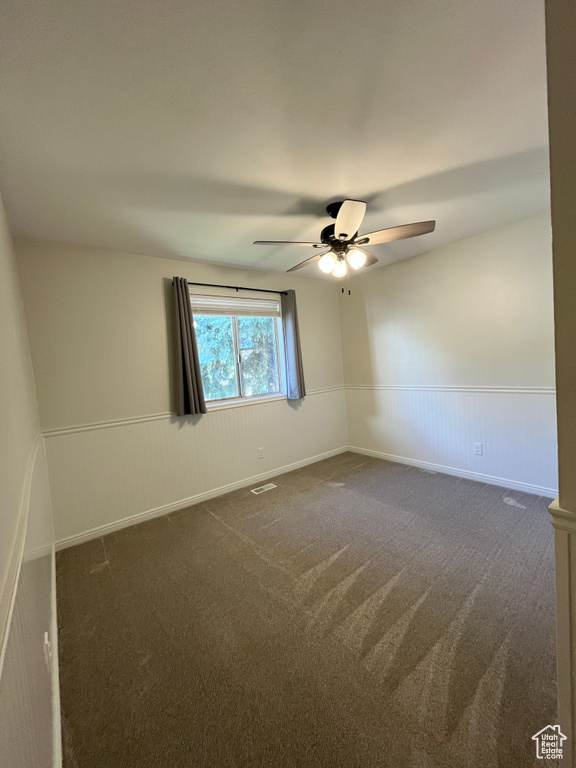 Spare room with a wainscoted wall, dark carpet, and a ceiling fan