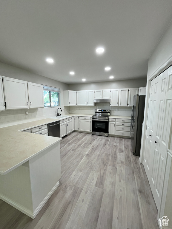 Kitchen with appliances with stainless steel finishes, light wood-style floors, a peninsula, under cabinet range hood, and tasteful backsplash