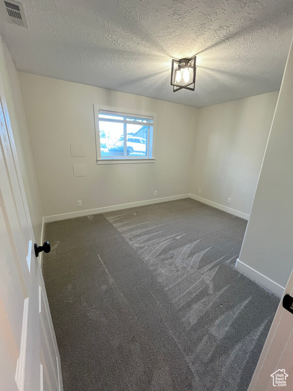 Empty room with dark colored carpet and a textured ceiling