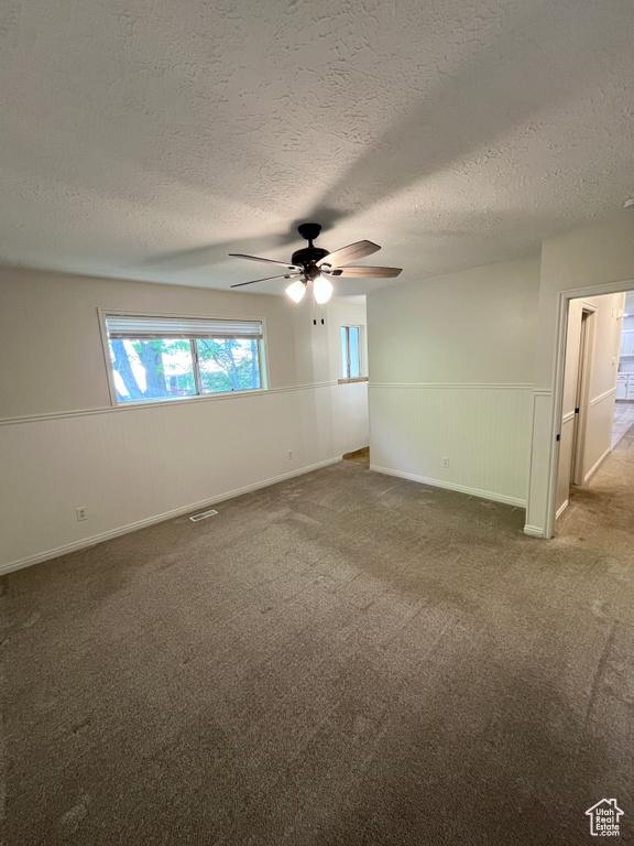 Carpeted spare room featuring ceiling fan, a wainscoted wall, and a textured ceiling