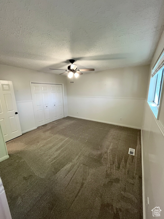 Unfurnished bedroom with a wainscoted wall, a textured ceiling, carpet flooring, a ceiling fan, and a closet