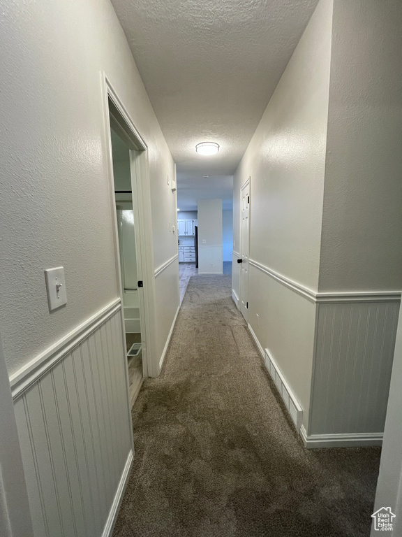 Hall featuring a textured ceiling, carpet flooring, and a textured wall
