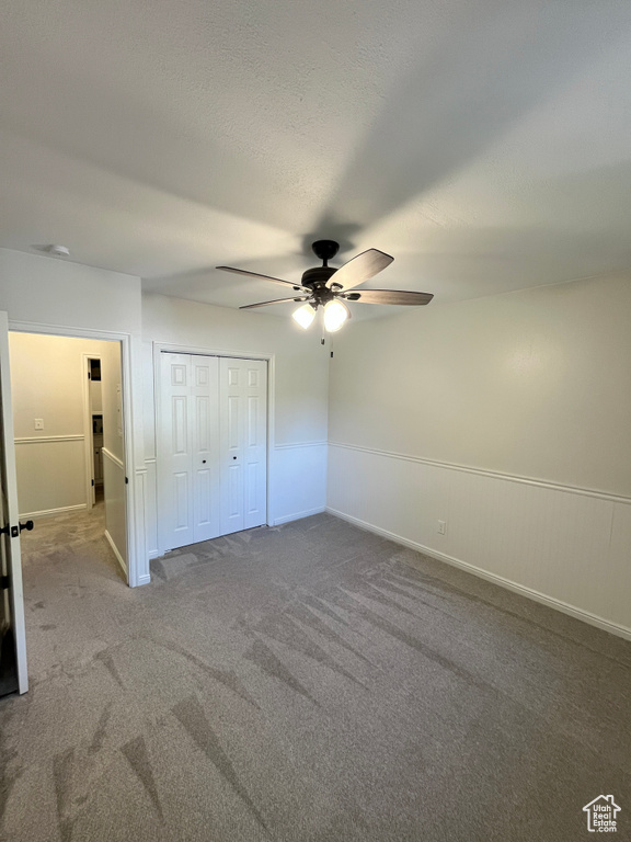 Unfurnished bedroom with carpet, a ceiling fan, a closet, and a wainscoted wall