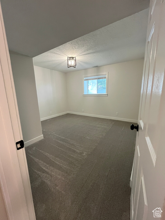 Unfurnished room featuring dark colored carpet and a textured ceiling