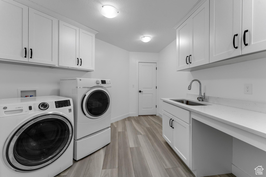 Laundry area with washer and clothes dryer, cabinet space, and light wood-type flooring