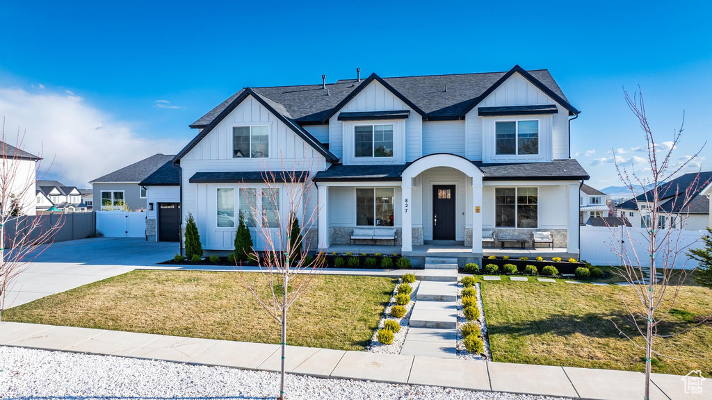 View of front of home with board and batten siding, a gate, concrete driveway, covered porch, and a shingled roof