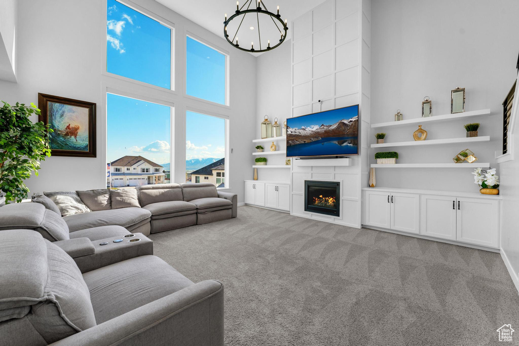 Living area with a high ceiling, a chandelier, light carpet, built in features, and a fireplace