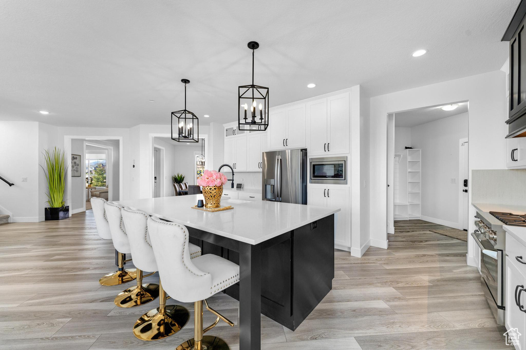 Kitchen with stainless steel appliances, light countertops, recessed lighting, white cabinets, and a kitchen island with sink