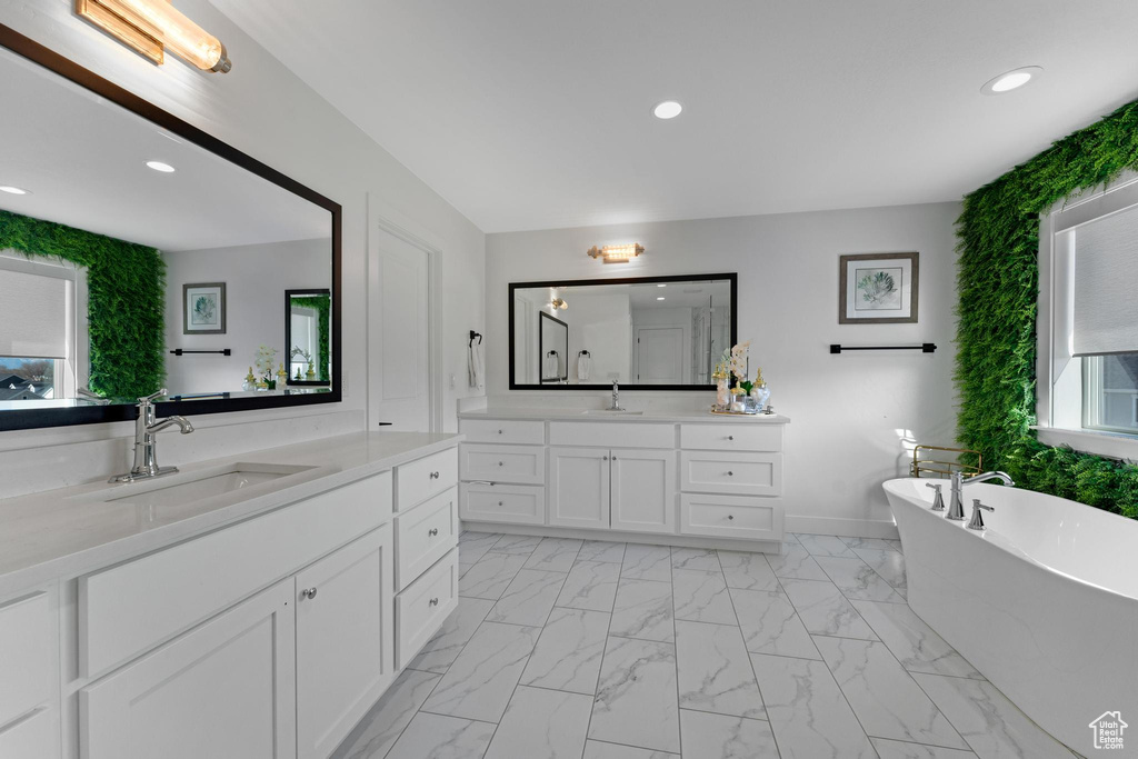 Full bath featuring marble finish floors, two vanities, a soaking tub, and recessed lighting