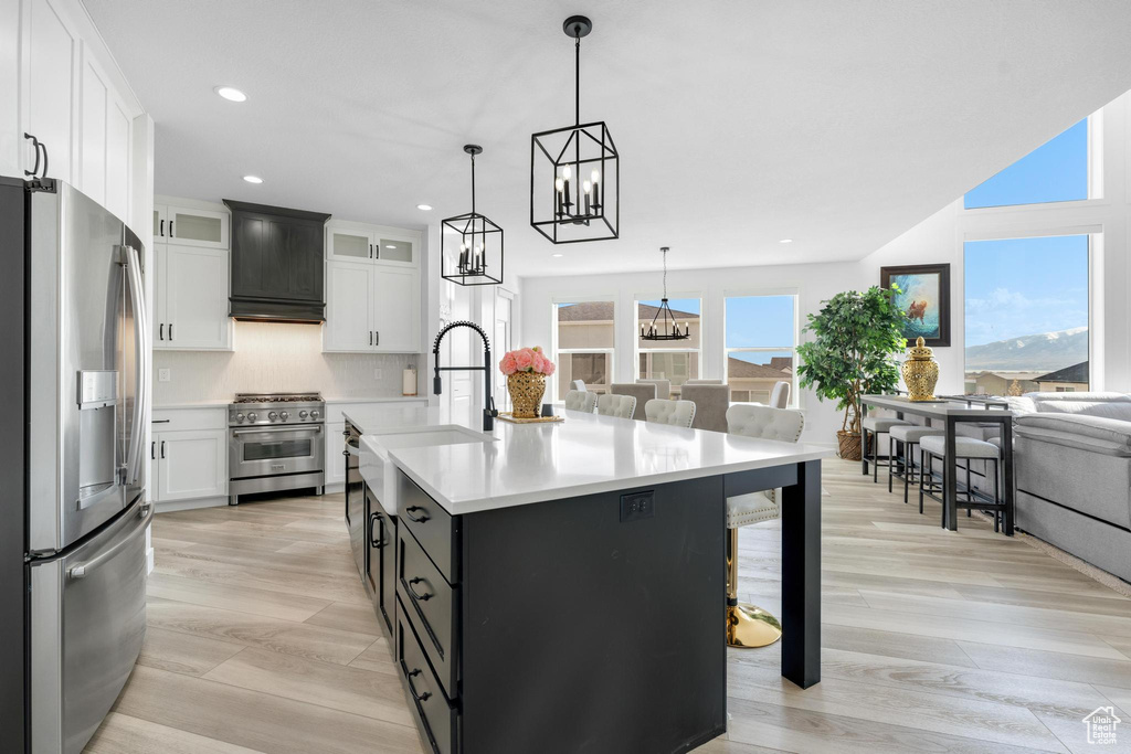 Kitchen with appliances with stainless steel finishes, premium range hood, open floor plan, a chandelier, and light countertops