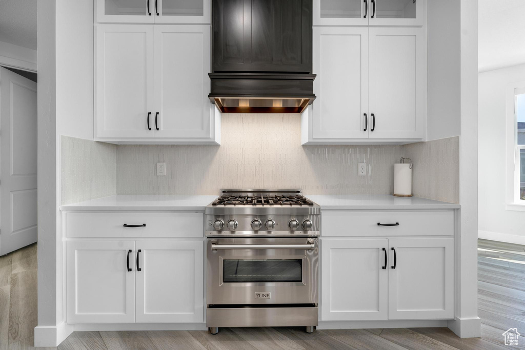 Kitchen with high end stainless steel range, extractor fan, light countertops, and white cabinets