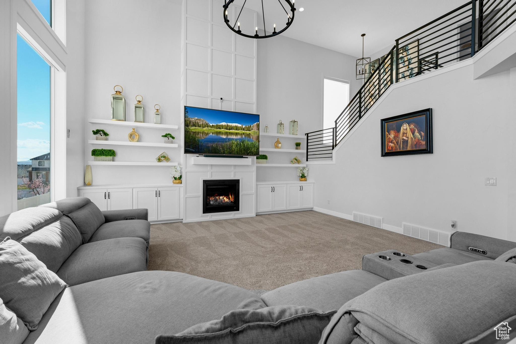 Living area with a towering ceiling, a chandelier, carpet, and a large fireplace