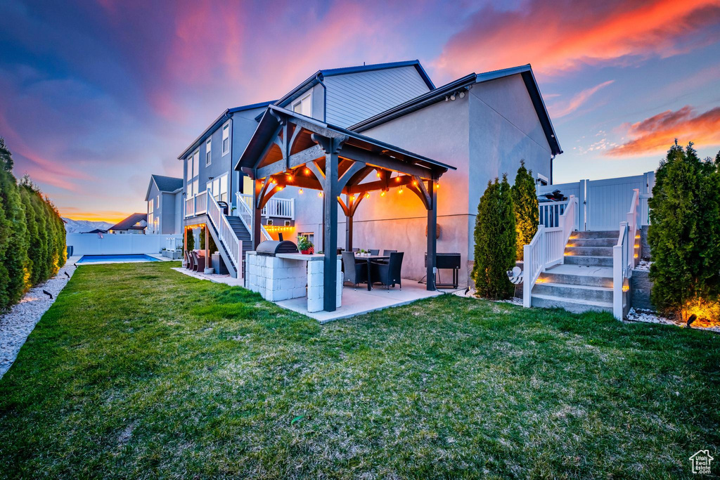 Back of property at dusk featuring stairs, a patio area, a fenced backyard, stucco siding, and a deck