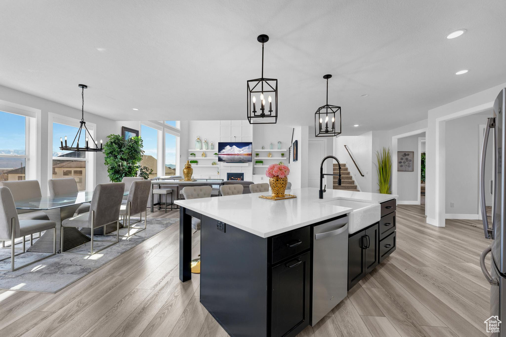 Kitchen featuring stainless steel appliances, dark cabinets, a chandelier, light wood-type flooring, and light countertops