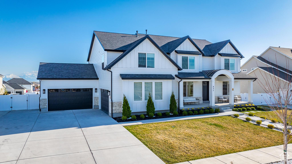 Modern inspired farmhouse with a gate, board and batten siding, an attached garage, concrete driveway, and covered porch