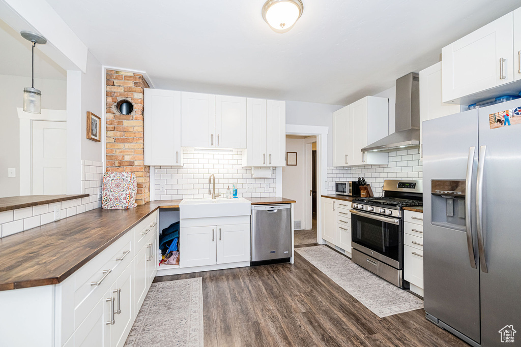 Kitchen featuring stainless steel appliances, wall chimney exhaust hood, wood counters, backsplash, and dark wood-style floors