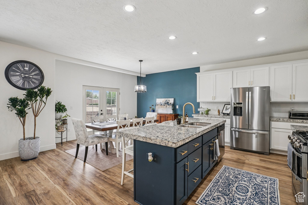 Kitchen featuring stainless steel appliances, white cabinets, recessed lighting, wood finished floors, and a kitchen island with sink