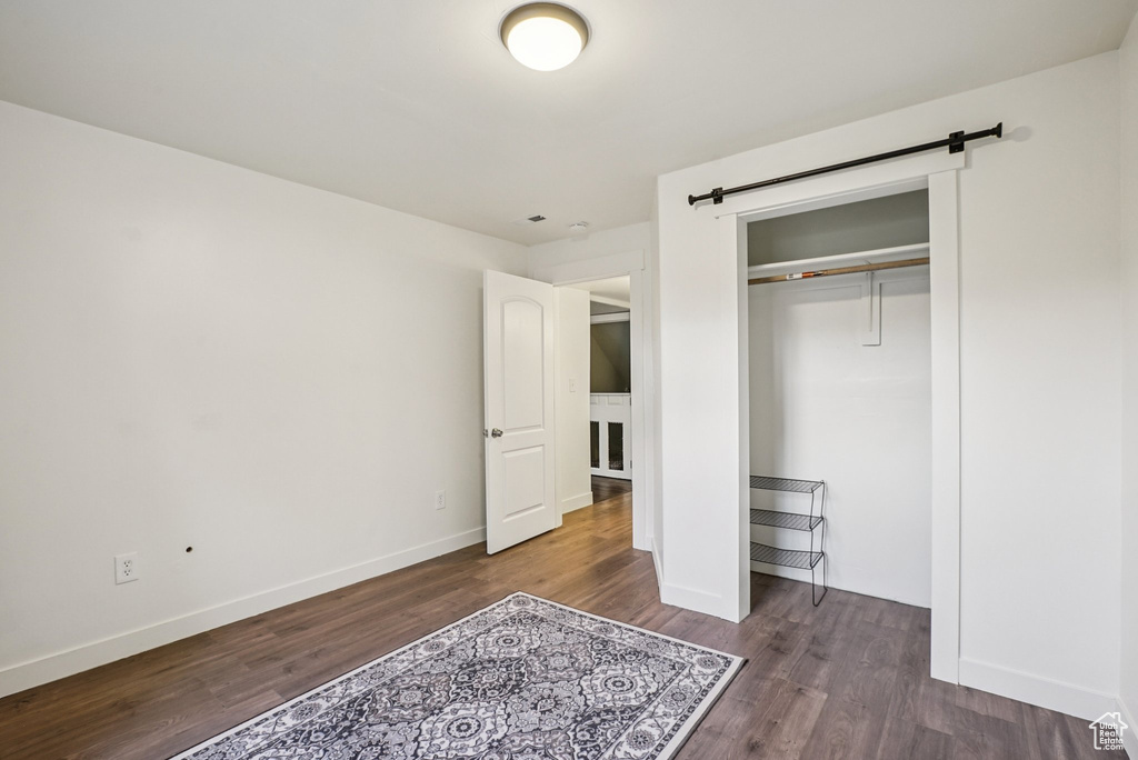 Unfurnished bedroom featuring wood finished floors, a closet, and a barn door