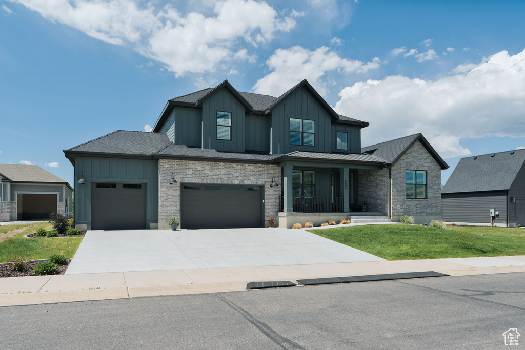 View of front of house featuring board and batten siding, a front yard, an attached garage, driveway, and brick siding
