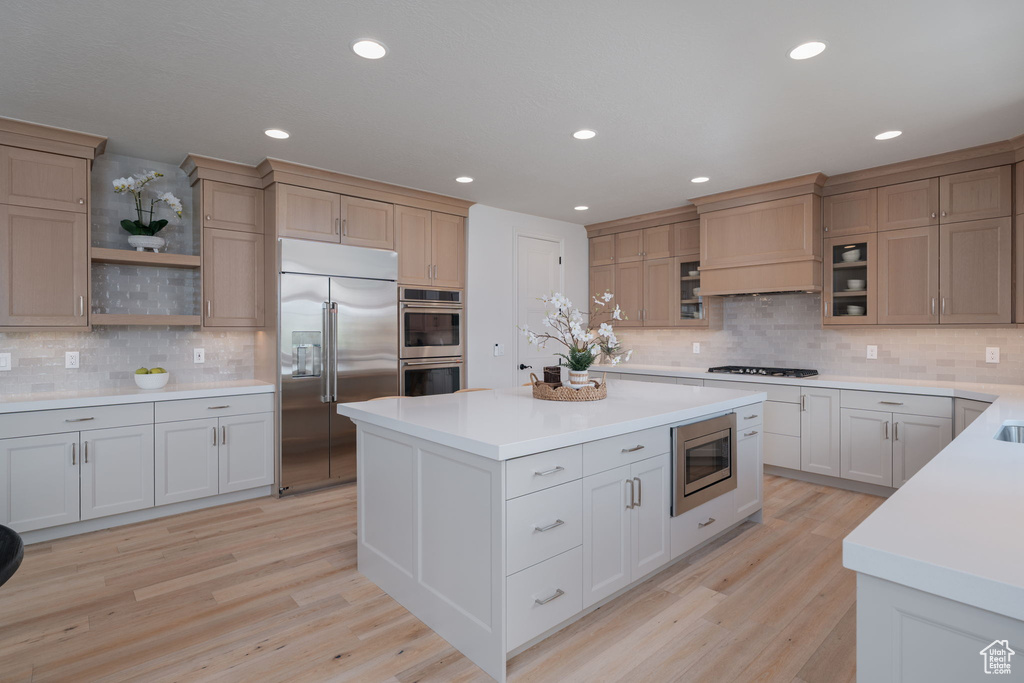 Kitchen with built in appliances, tasteful backsplash, light countertops, a center island, and recessed lighting