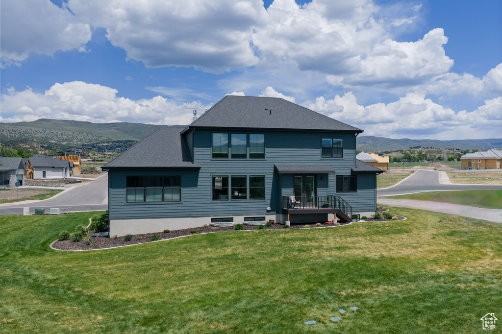 Rear view of house with a mountain view, a lawn, and roof with shingles