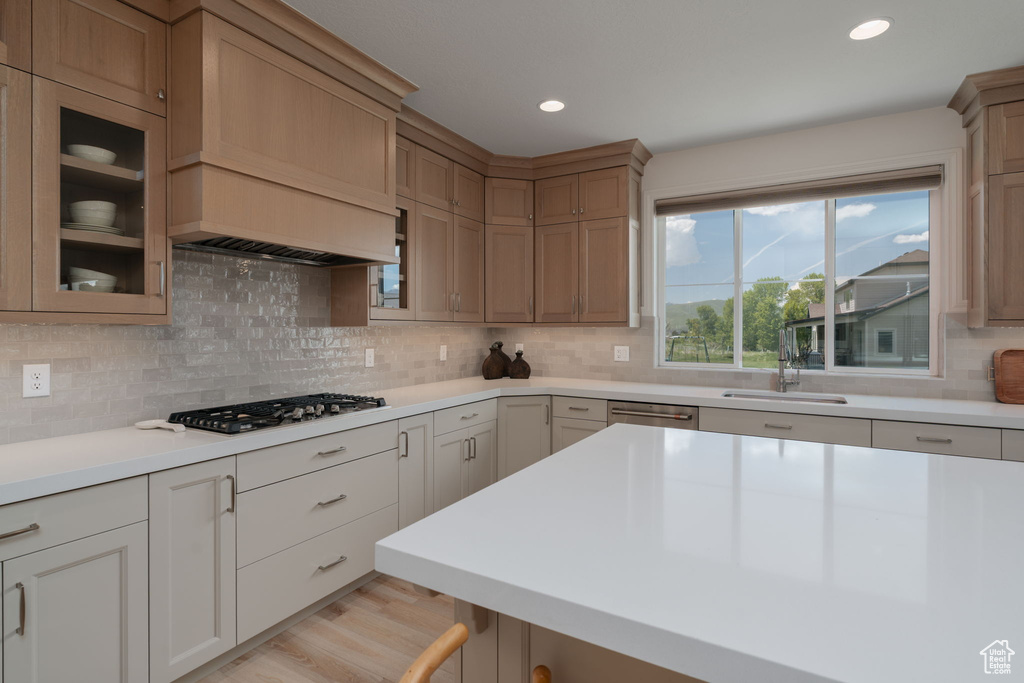 Kitchen with stainless steel appliances, light countertops, backsplash, glass insert cabinets, and recessed lighting