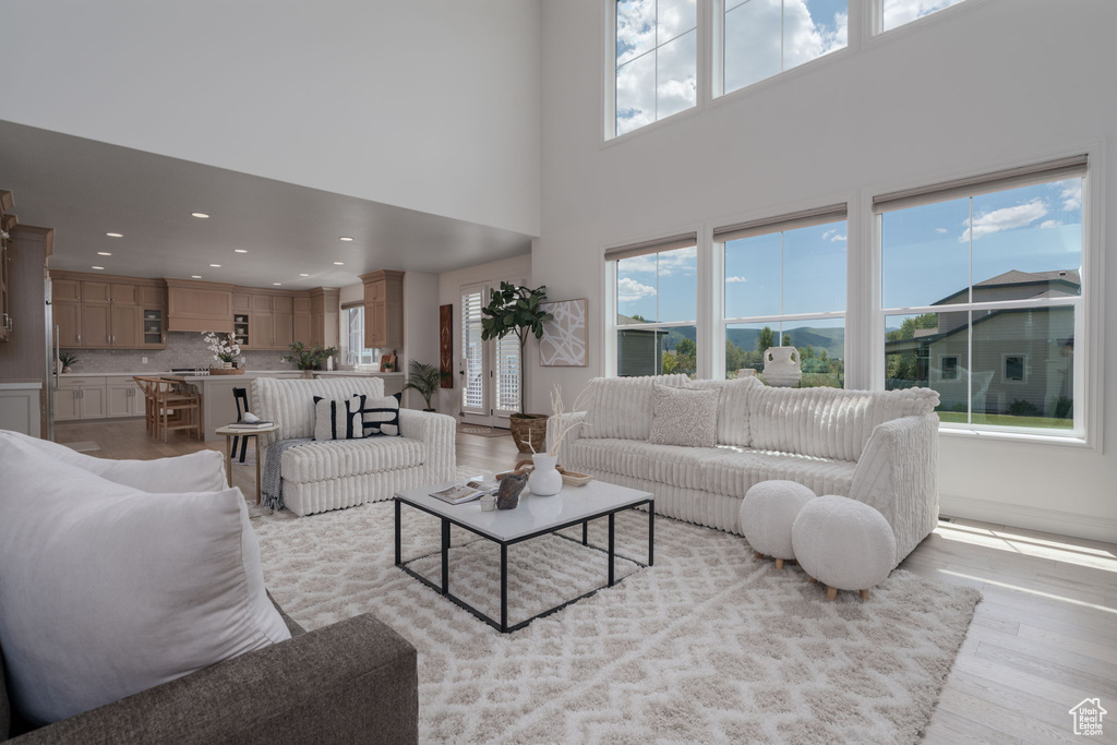 Living area with healthy amount of natural light, light wood-type flooring, recessed lighting, and a towering ceiling