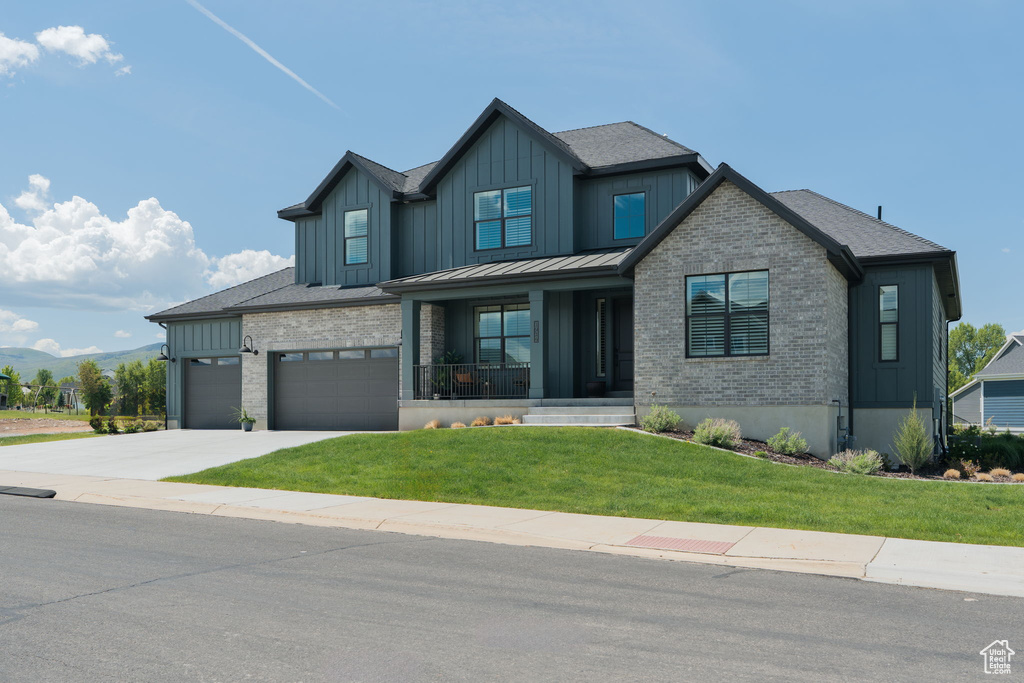 Modern farmhouse featuring board and batten siding, a front yard, a porch, driveway, and brick siding