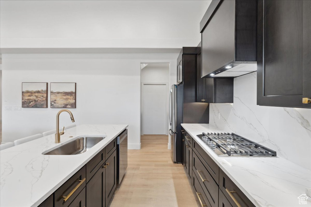Kitchen featuring appliances with stainless steel finishes, light wood finished floors, light stone counters, and decorative backsplash