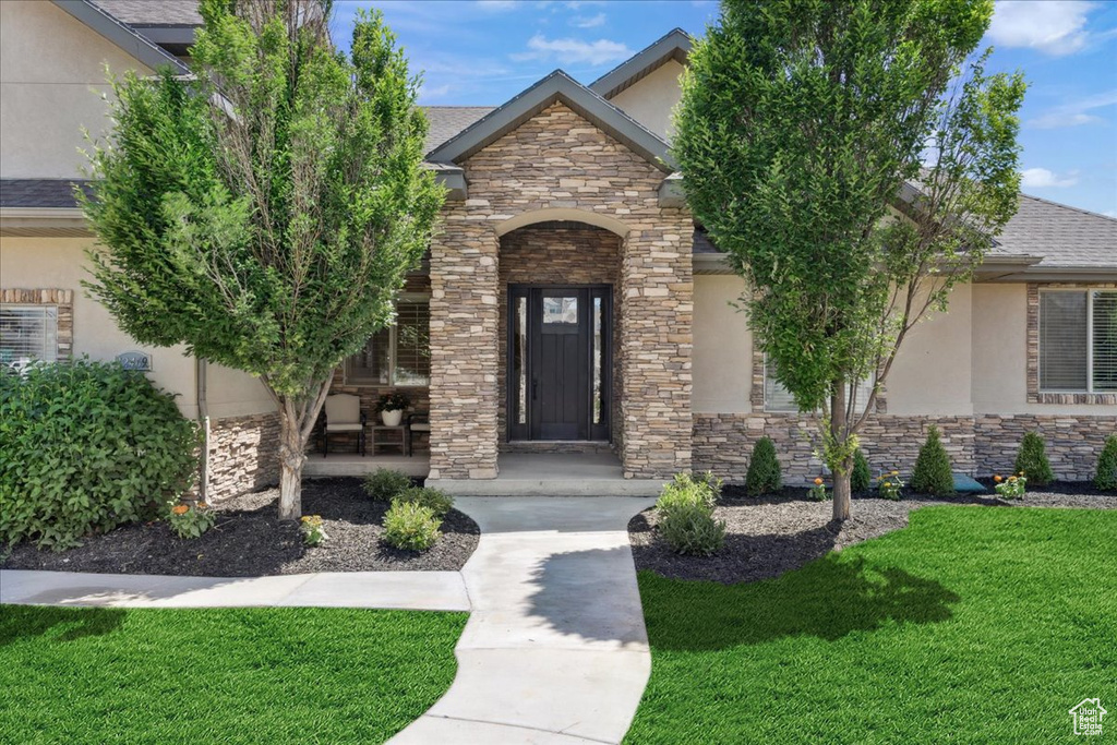 View of front of property featuring stone siding, stucco siding, a front yard, and a porch