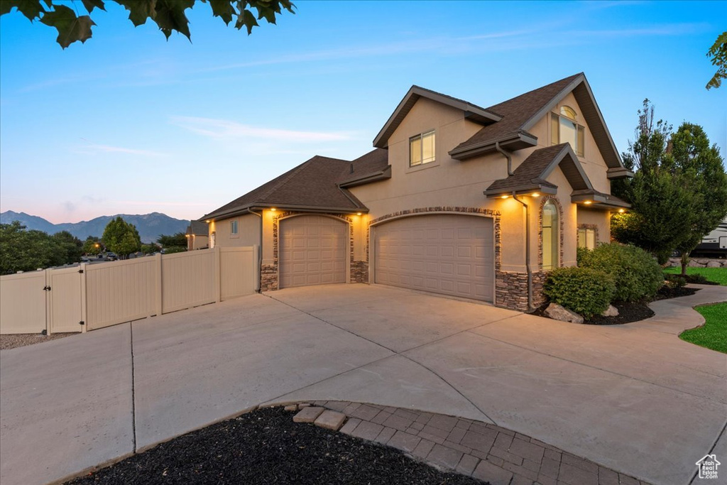 View of front facade with concrete driveway, an attached garage, a gate, stucco siding, and stone siding