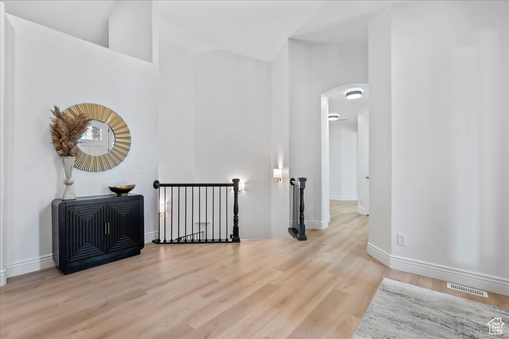 Hall with an upstairs landing, arched walkways, wood finished floors, and high vaulted ceiling