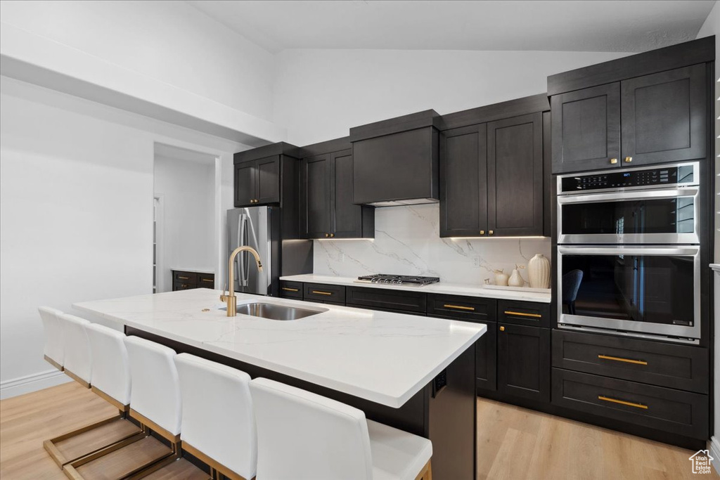 Kitchen with appliances with stainless steel finishes, vaulted ceiling, light wood-type flooring, decorative backsplash, and a kitchen breakfast bar