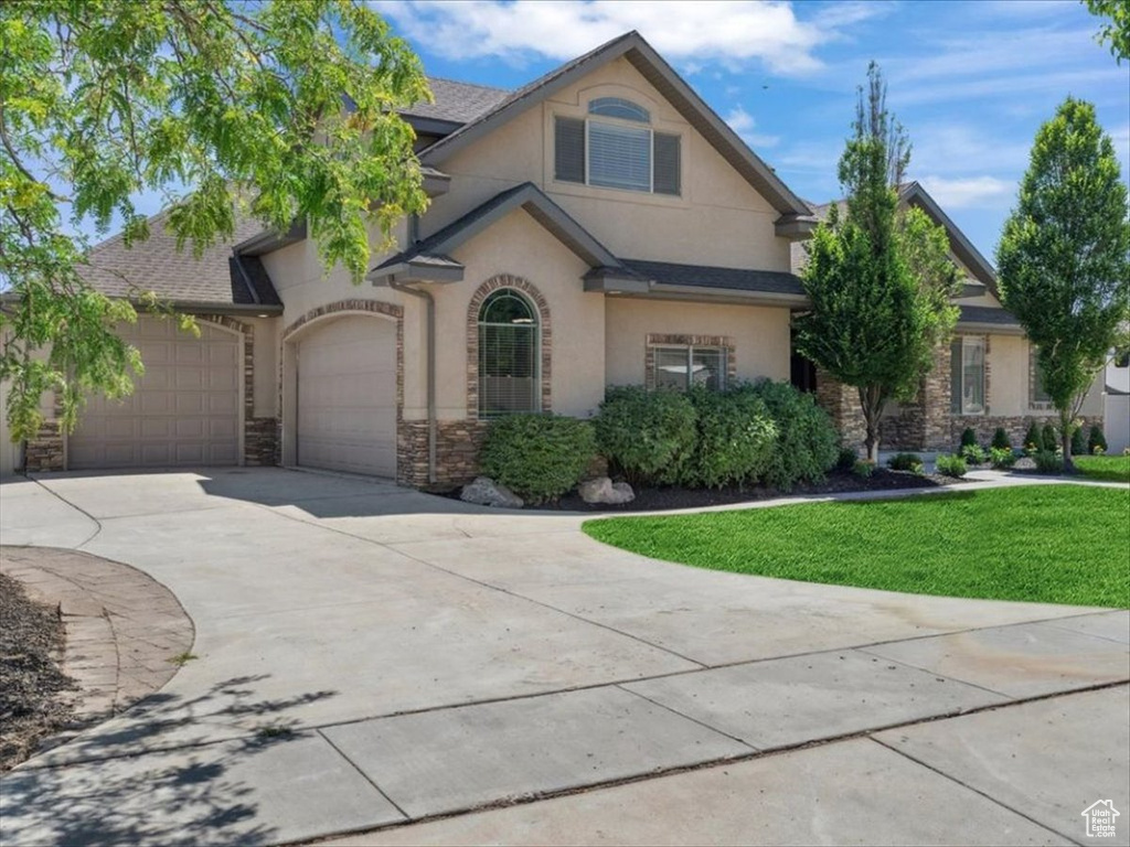 View of front of home with stone siding, an attached garage, stucco siding, driveway, and a front lawn