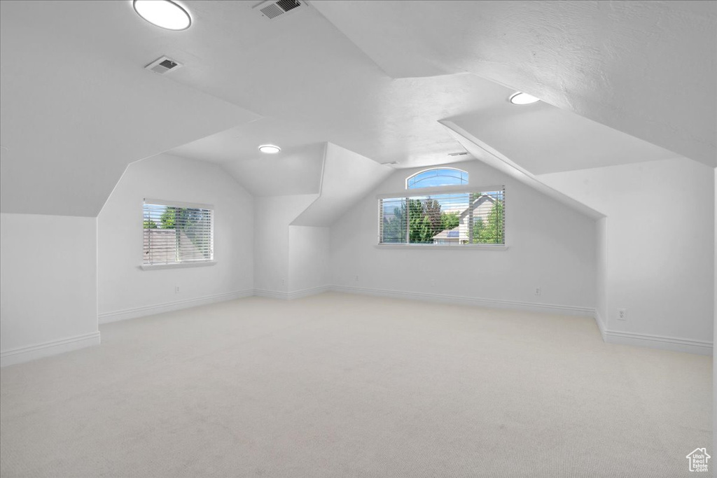 Additional living space with light colored carpet, healthy amount of natural light, and vaulted ceiling