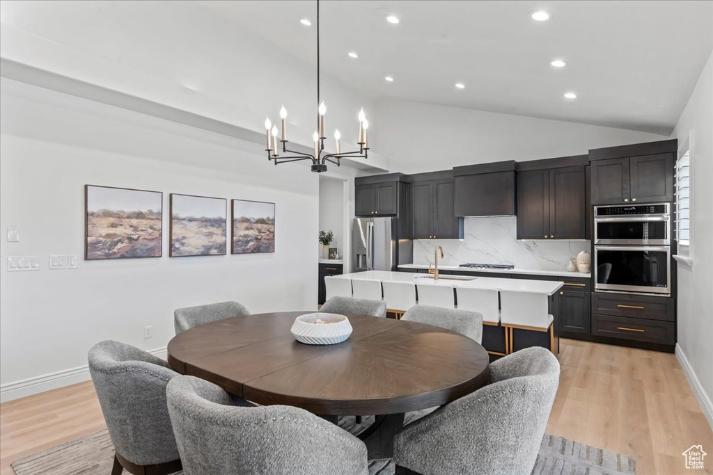 Dining room with a chandelier, vaulted ceiling, light wood-style floors, and recessed lighting