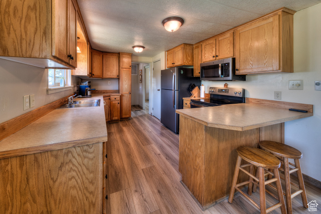 Kitchen featuring appliances with stainless steel finishes, a peninsula, light wood finished floors, and light countertops